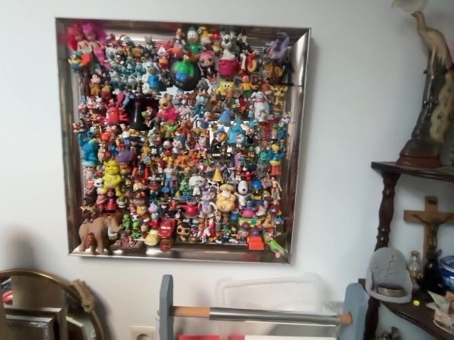Ingelijste collage van vele kleurrijke beeldjes aan de muur boven woondecoratie en planken.