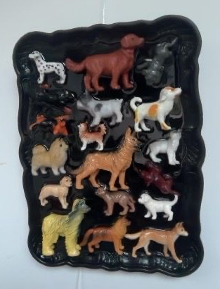 Diverse dierenbeeldjes, waaronder paarden, honden en een giraffe, staan ​​uitgestald op een zwart dienblad.