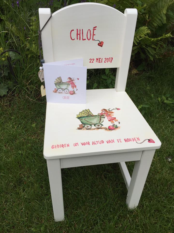 Witte stoel met “CHLOE” en “22 FEB 2020” erop geschilderd, versierd met kikkers in een groene buitenomgeving