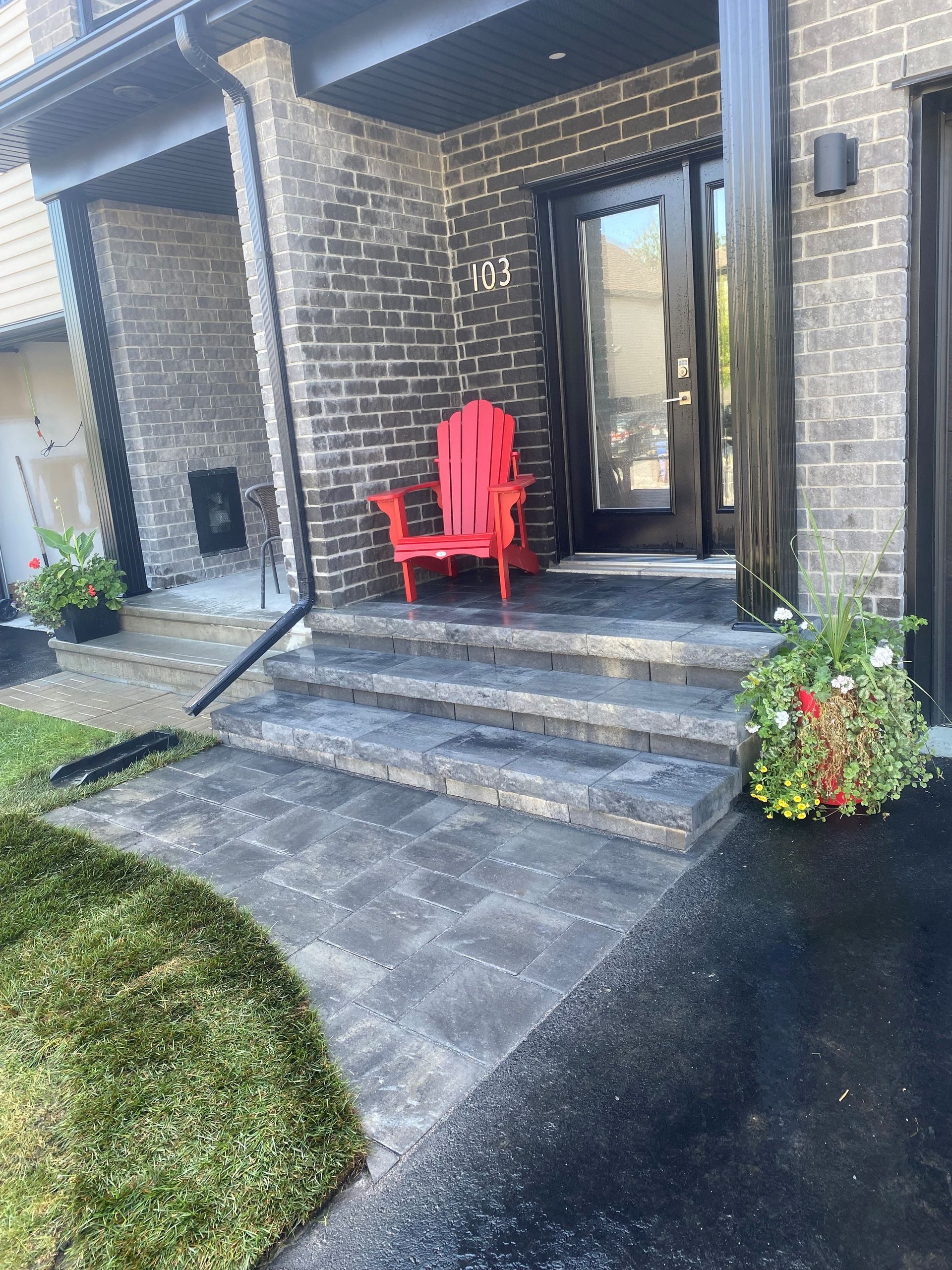 A red chair is sitting on the porch of a brick house.