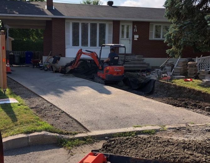 Une petite excavatrice orange est garée devant une maison