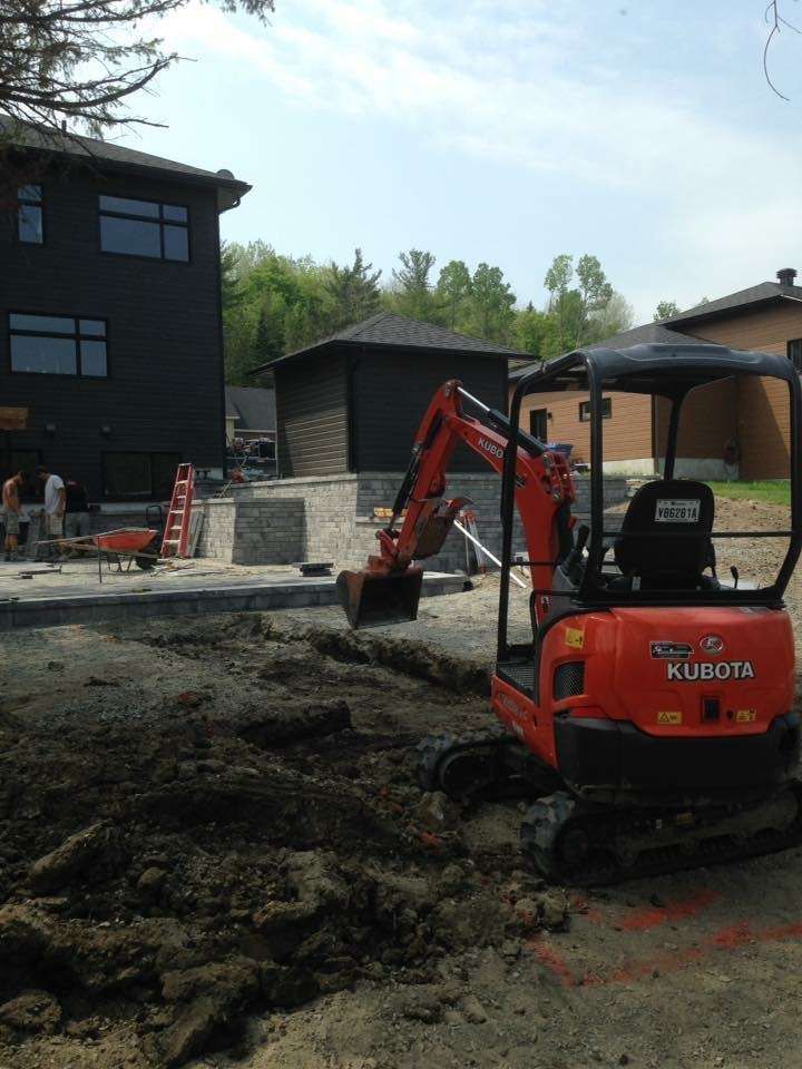 Une petite excavatrice Kubota orange est assise dans la terre devant une maison.