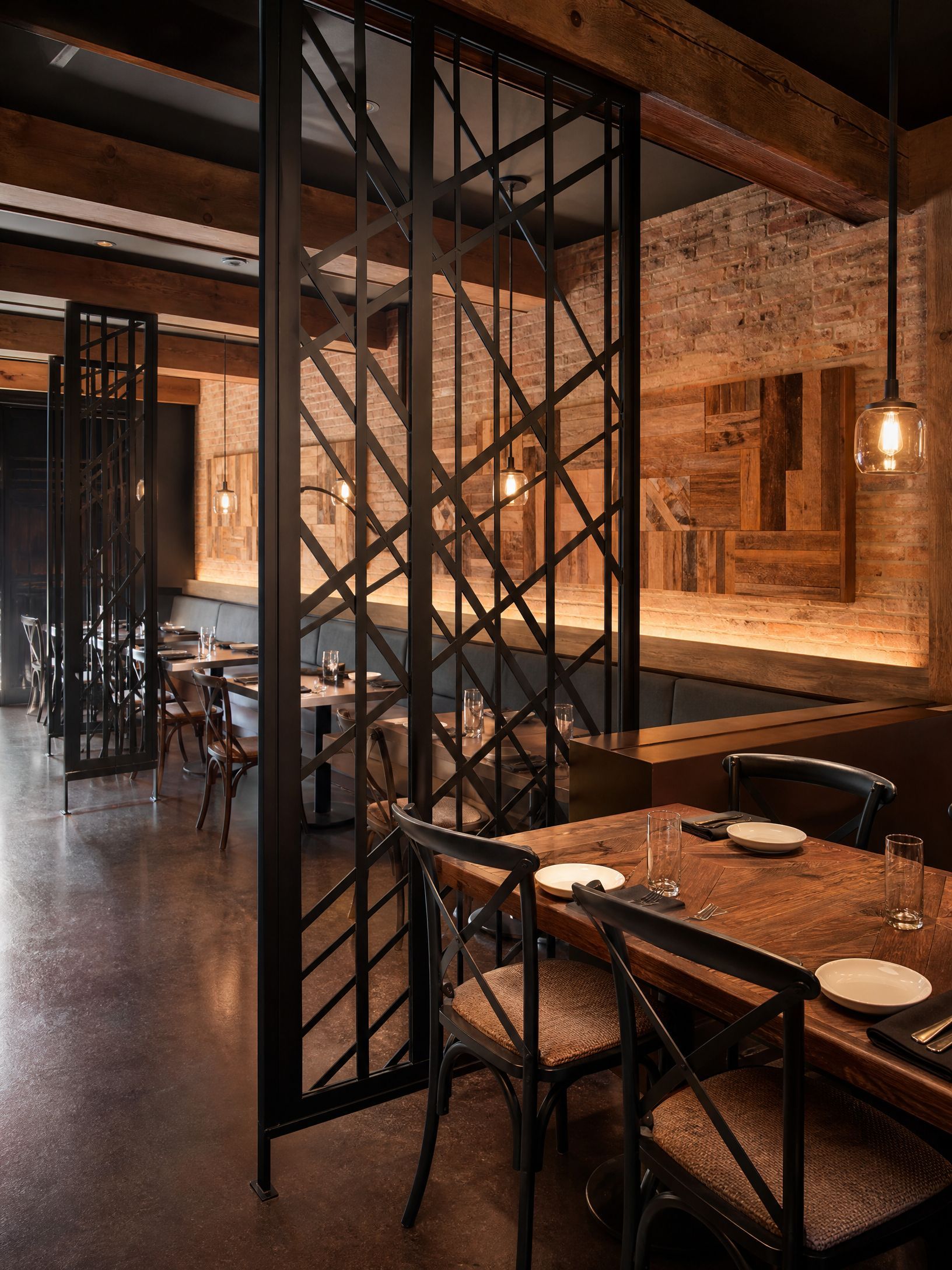 Rustic restaurant interior with brick walls, metal partition, and set wooden tables and chairs