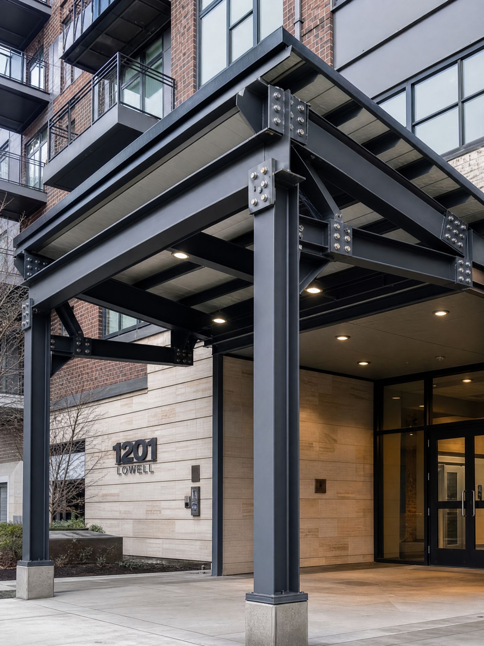 Modern apartment building entrance with a covered black steel canopy and glass doors