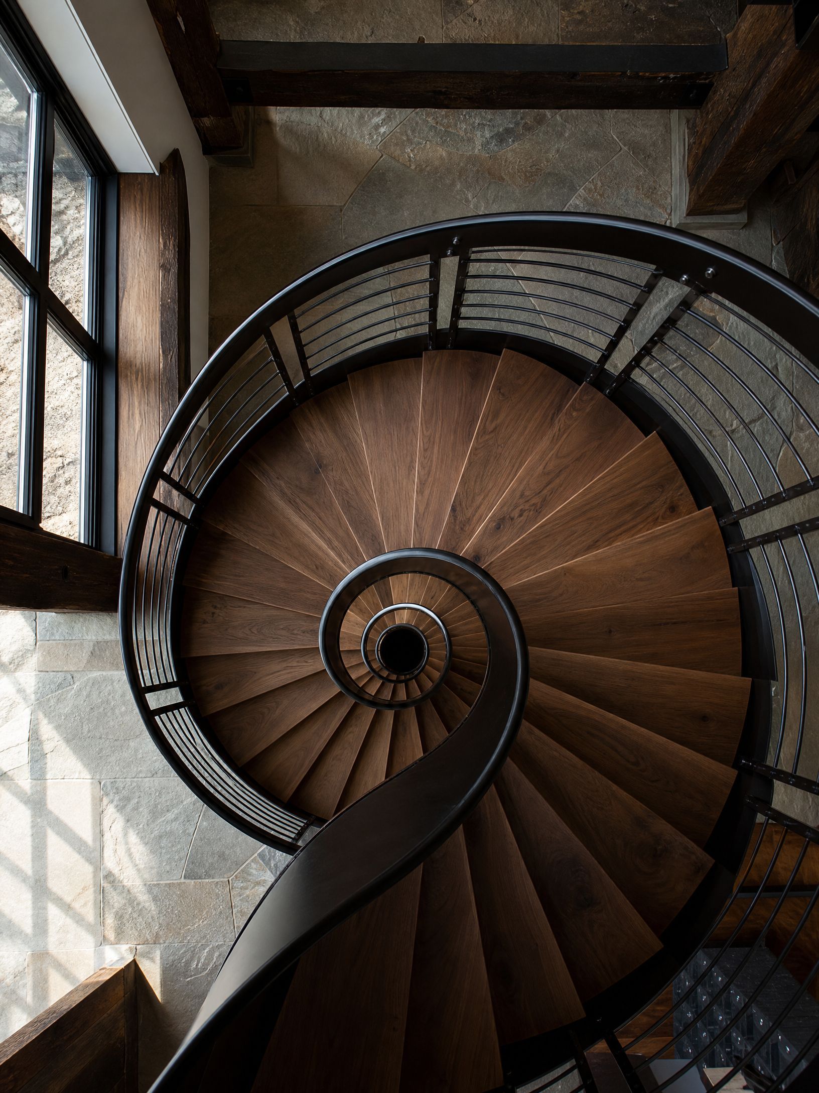 Spiral wooden staircase viewed from above, with metal railing and brick walls.