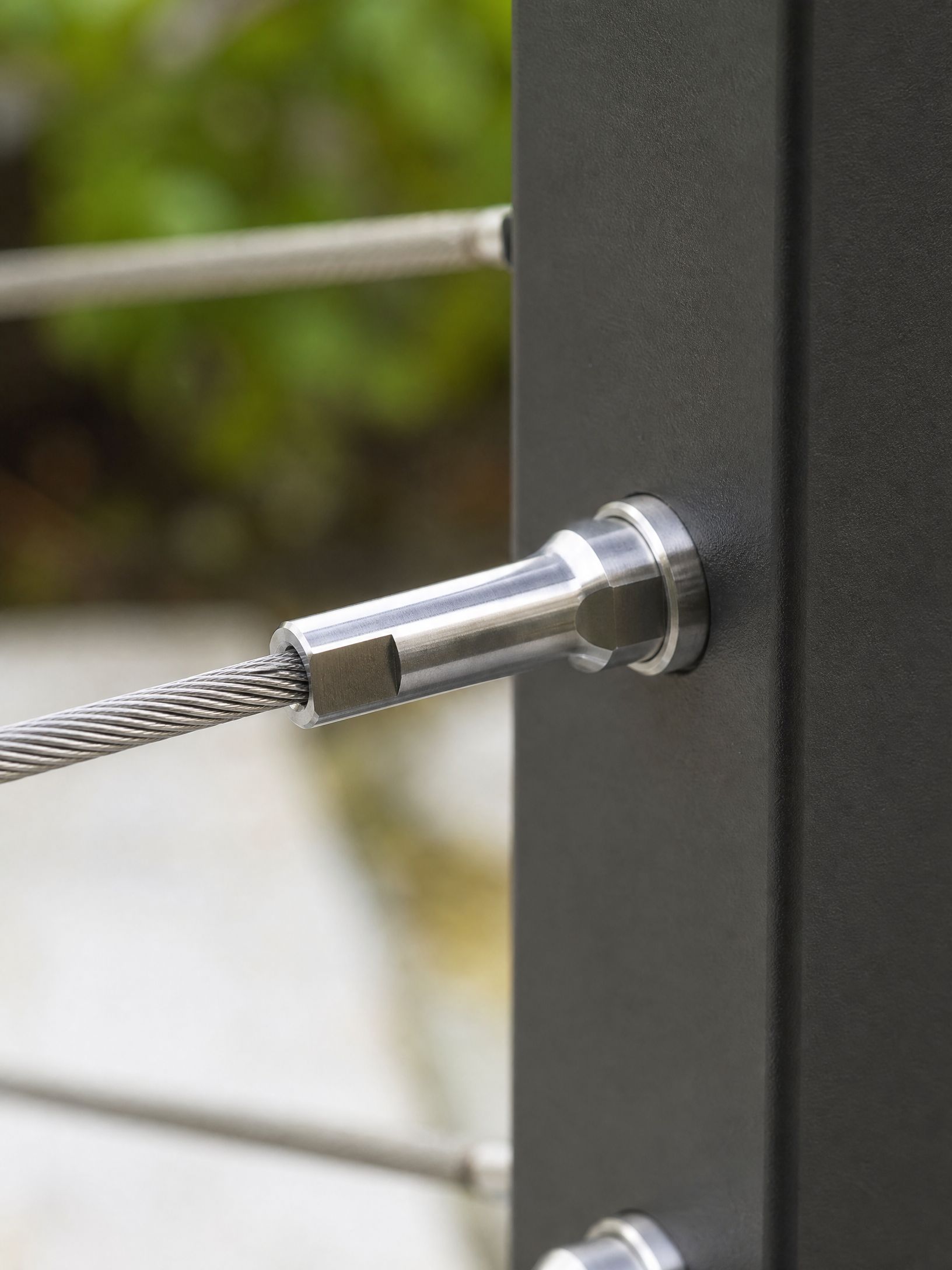 Close-up of a steel cable anchored to a dark metal post with a shiny fitting