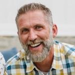 Smiling bearded man in a plaid shirt outdoors, looking at the camera