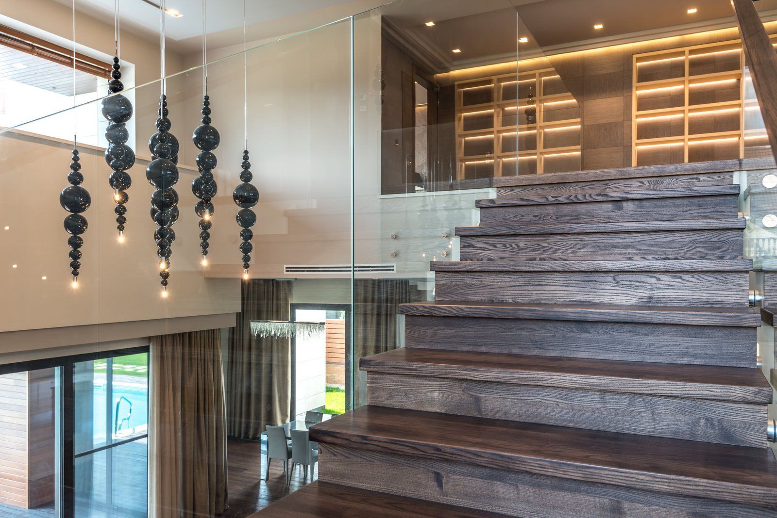 Dark wood stair treads beside tall frameless glass guard panels in a modern home interior