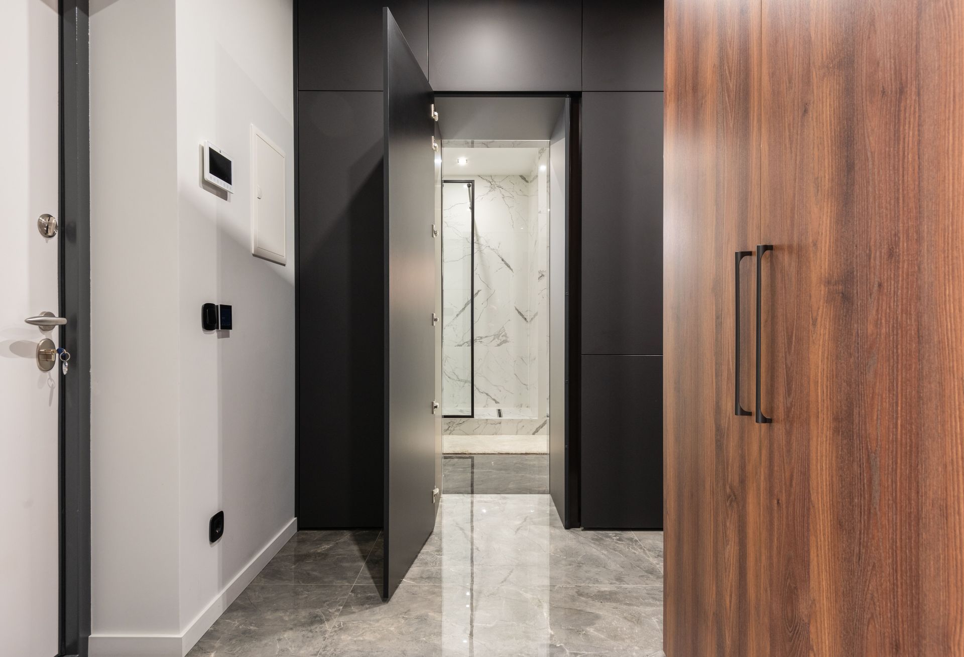 Modern hallway with dark walls, wood door, mirrored doorway, and marble floor.
