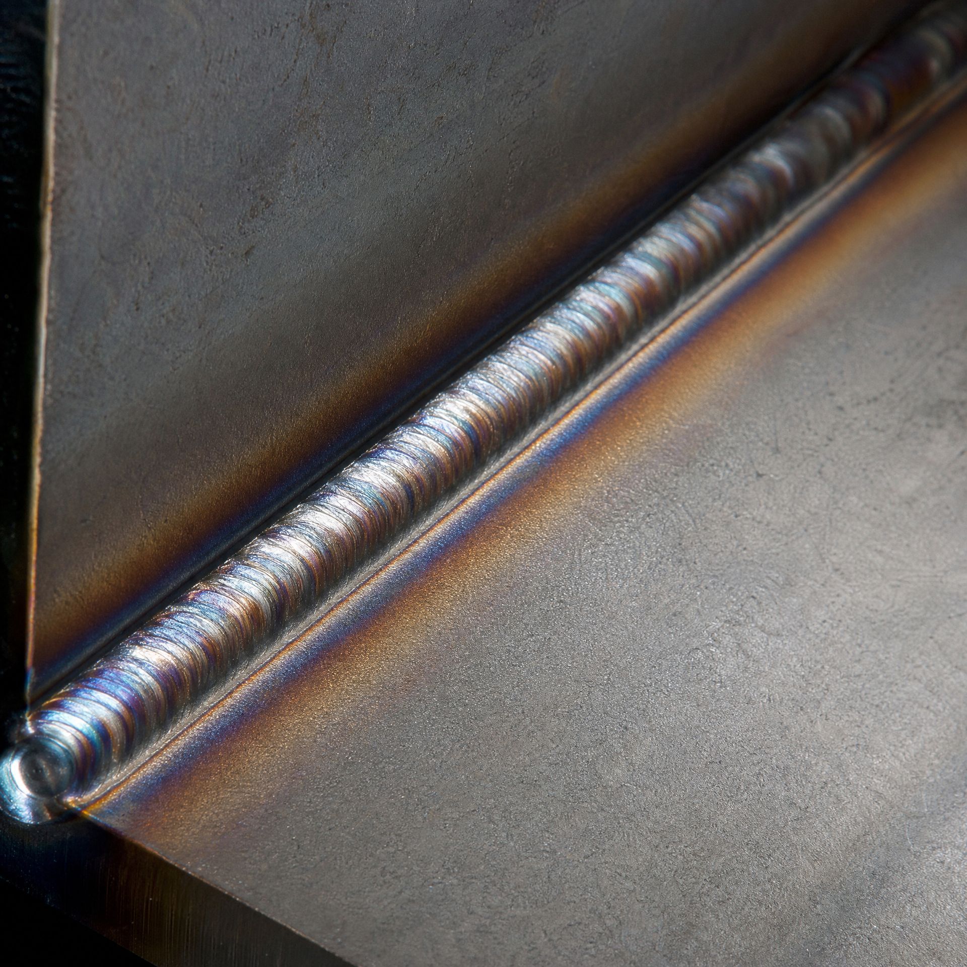 Close-up of a polished metal weld bead on a dark steel surface.