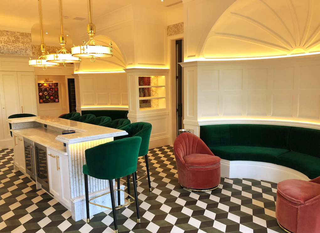 Retro diner with black-and-white checkered floor, green booths, pink chairs, and white bar stools under warm lights