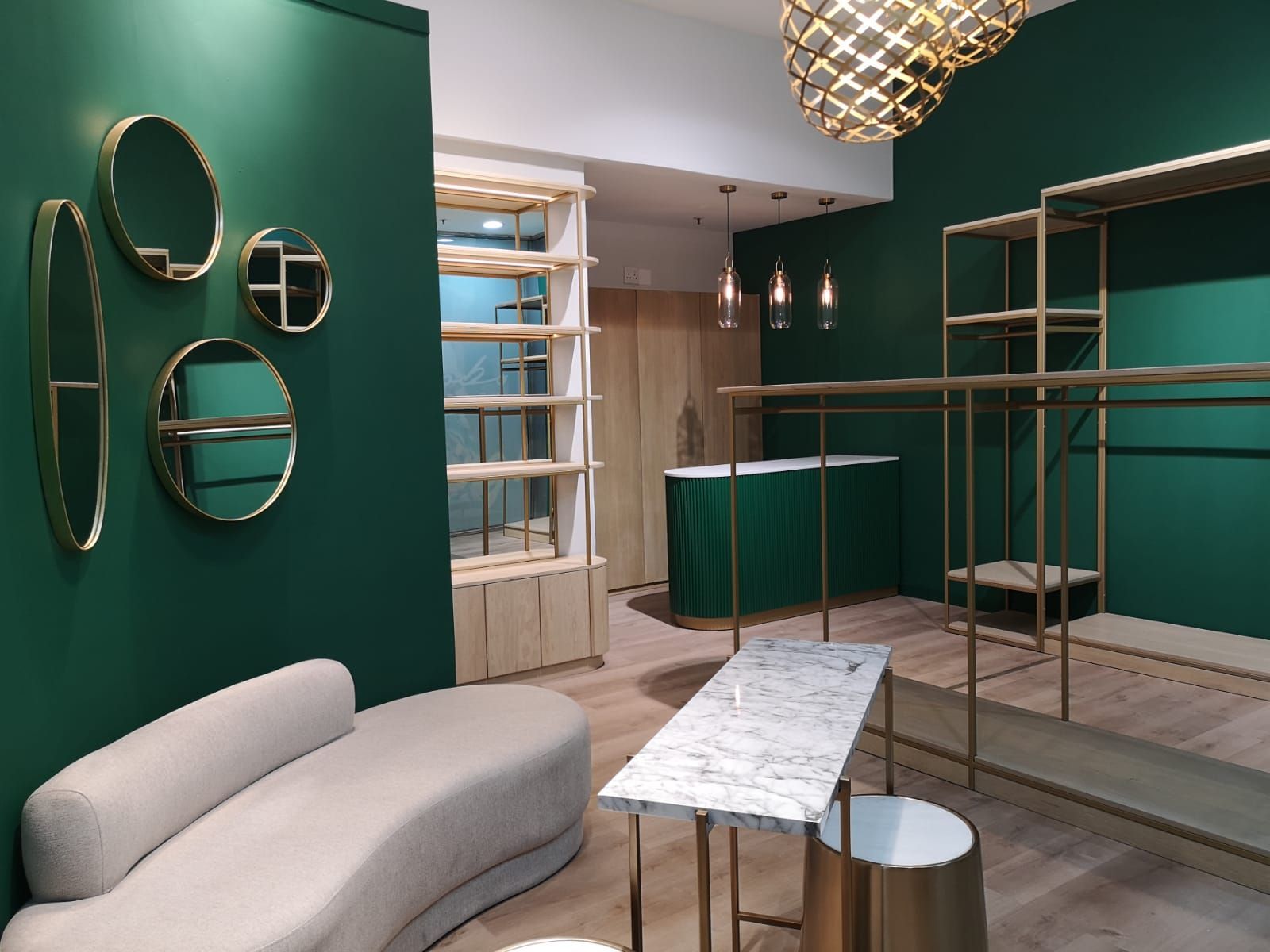 Green boutique showroom with mirrors, shelves, gold accents, and a marble table with a white bench
