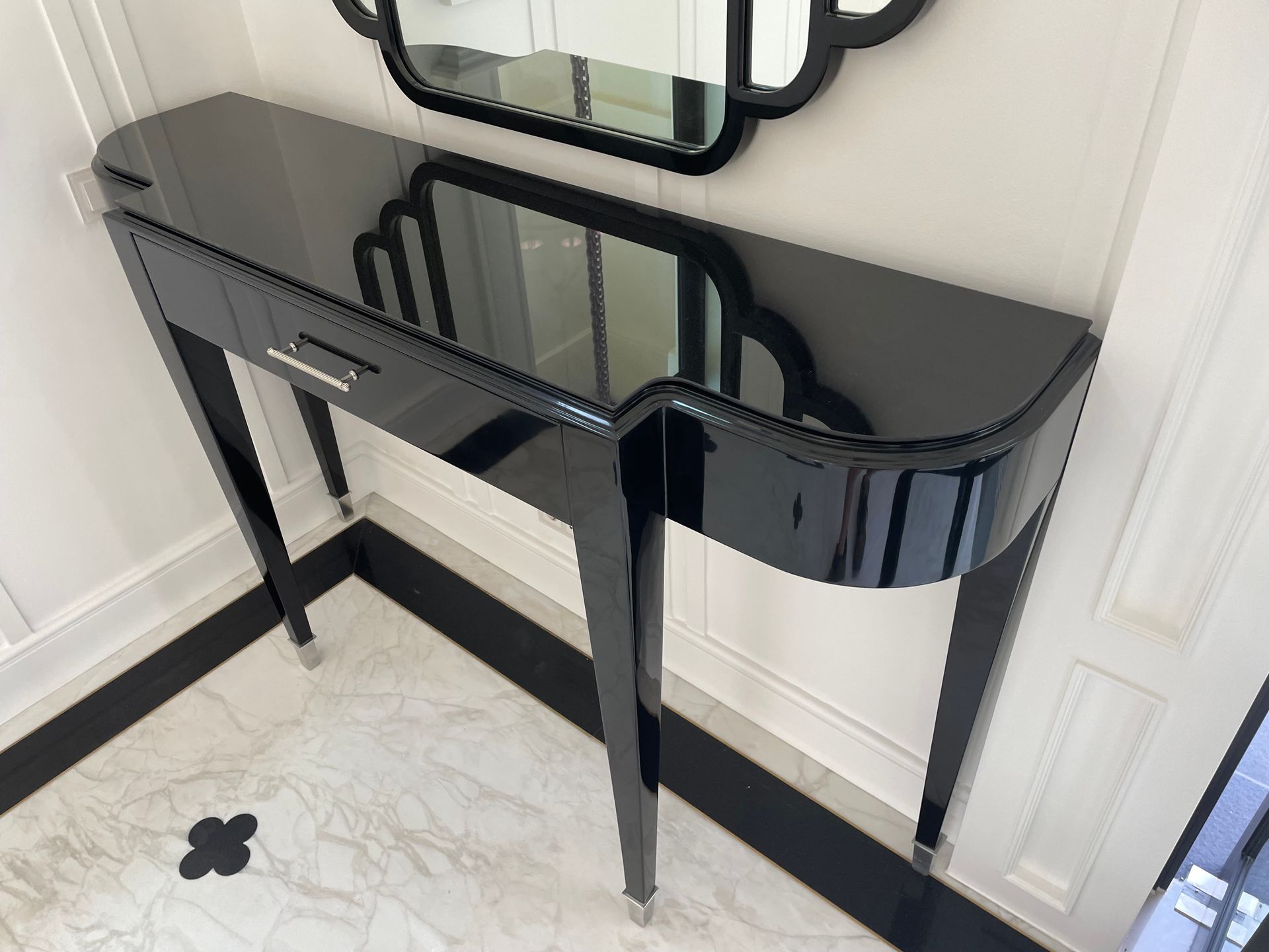 Black console table with drawer and mirror against white wall in a hallway