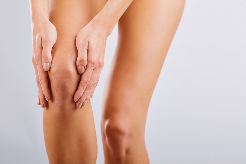 Woman holding both hands on a knee, indicating pain.