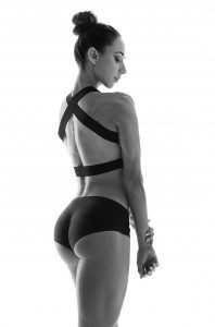 Woman in athletic wear, back to camera, bun hairstyle, studio setting.