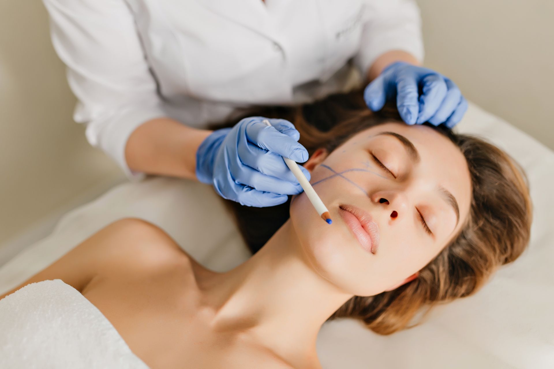 Woman in blue gloves injecting patient's lip, surrounded by observers, lit by overhead camera.