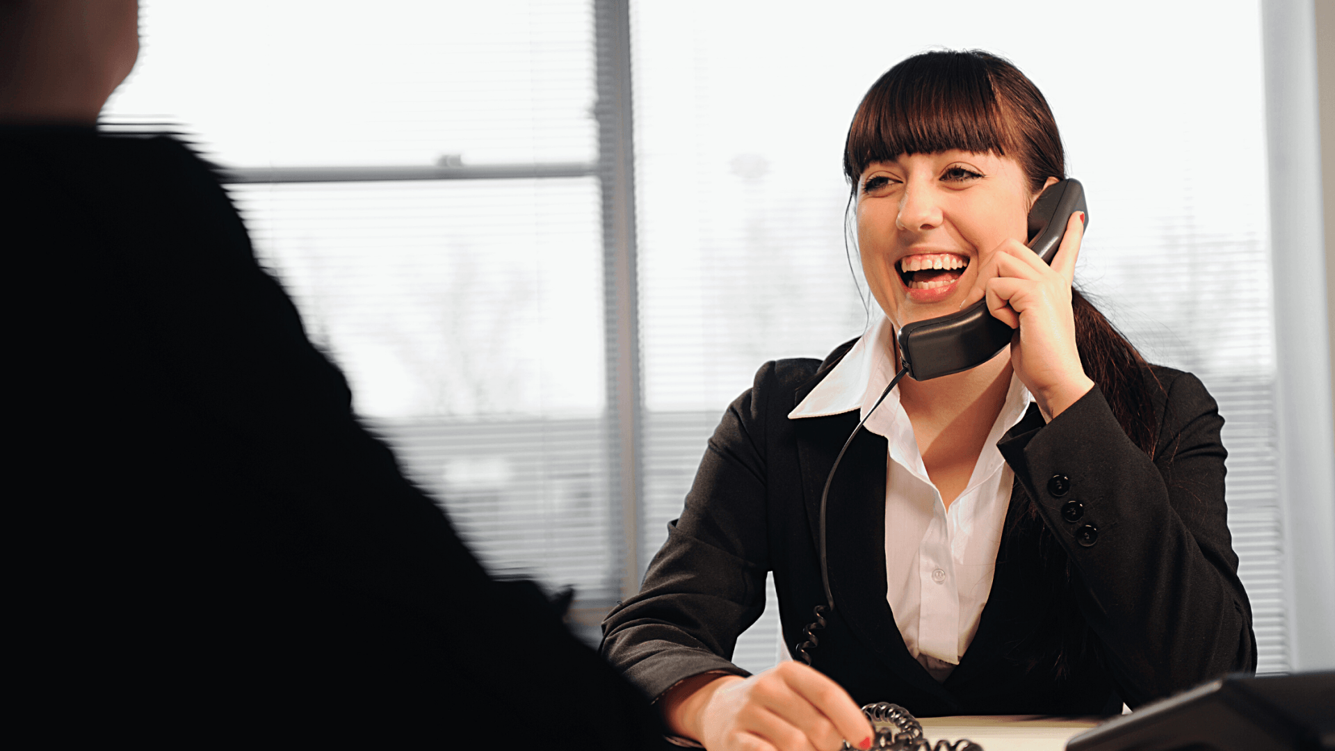 Office Manager smiling while answering patient call while another patient is at the front desk