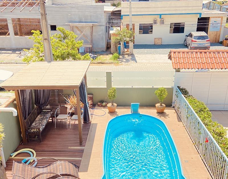 Uma piscina turquesa em um deck de madeira ao lado de um pátio coberto com assentos, vista de um ângulo elevado.