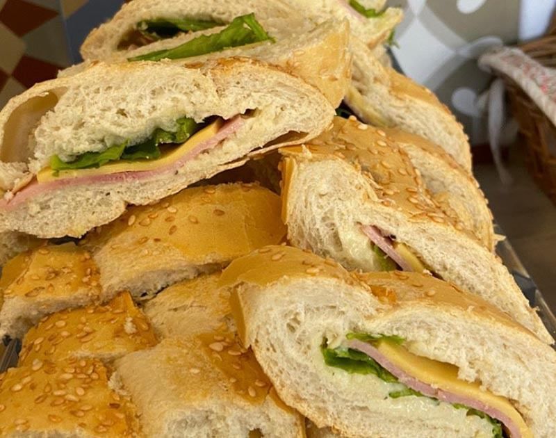 Uma imagem em close-up de vários sanduíches de presunto e queijo fatiados em pão com crosta de gergelim, dispostos em uma pilha.