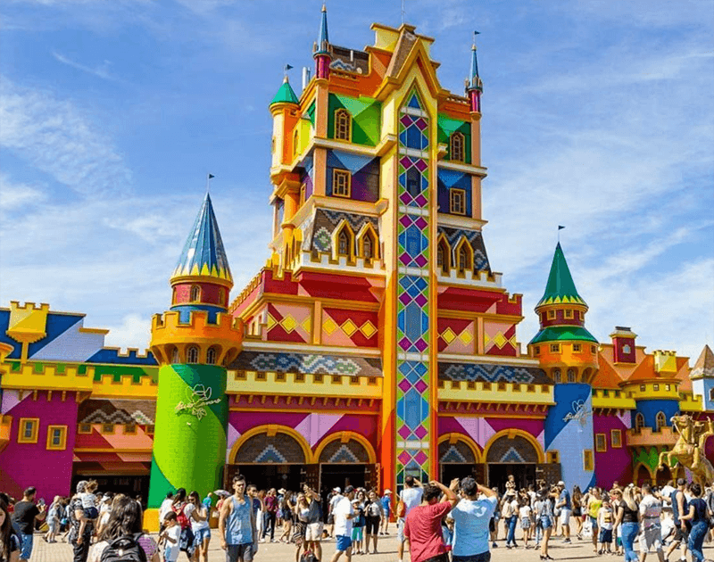 Castelo brilhante e colorido com torres e padrões geométricos no Beto Carrero World, com uma multidão de pessoas em frente.