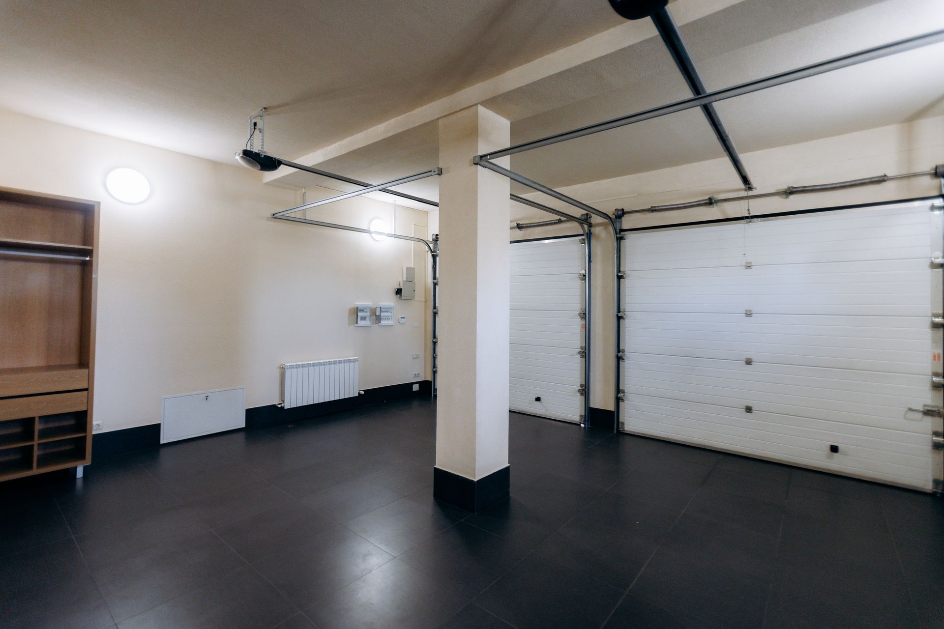 Empty garage interior with white walls, black floor, and closed white overhead door