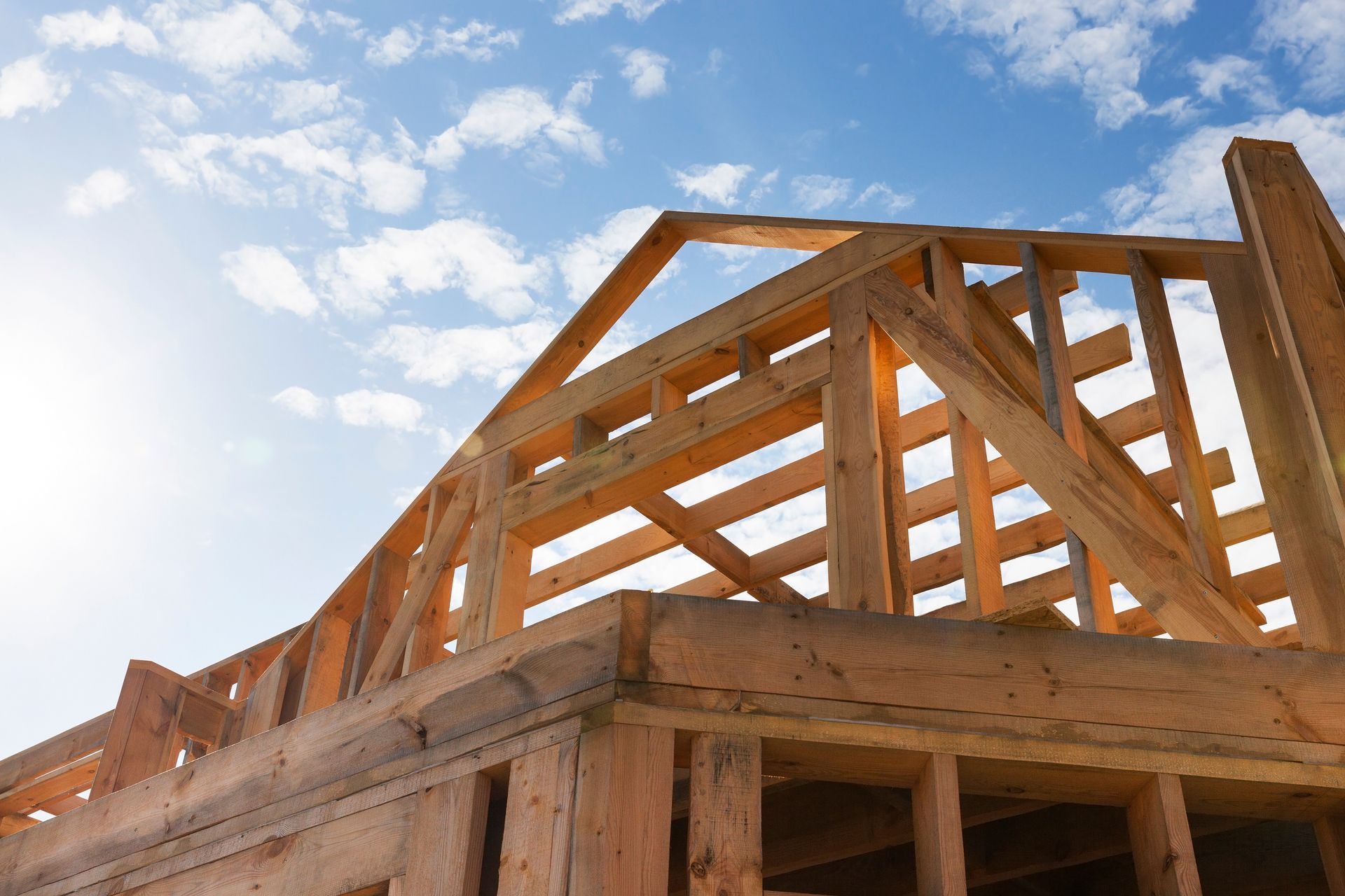Wooden house frame under construction against a blue sky with clouds