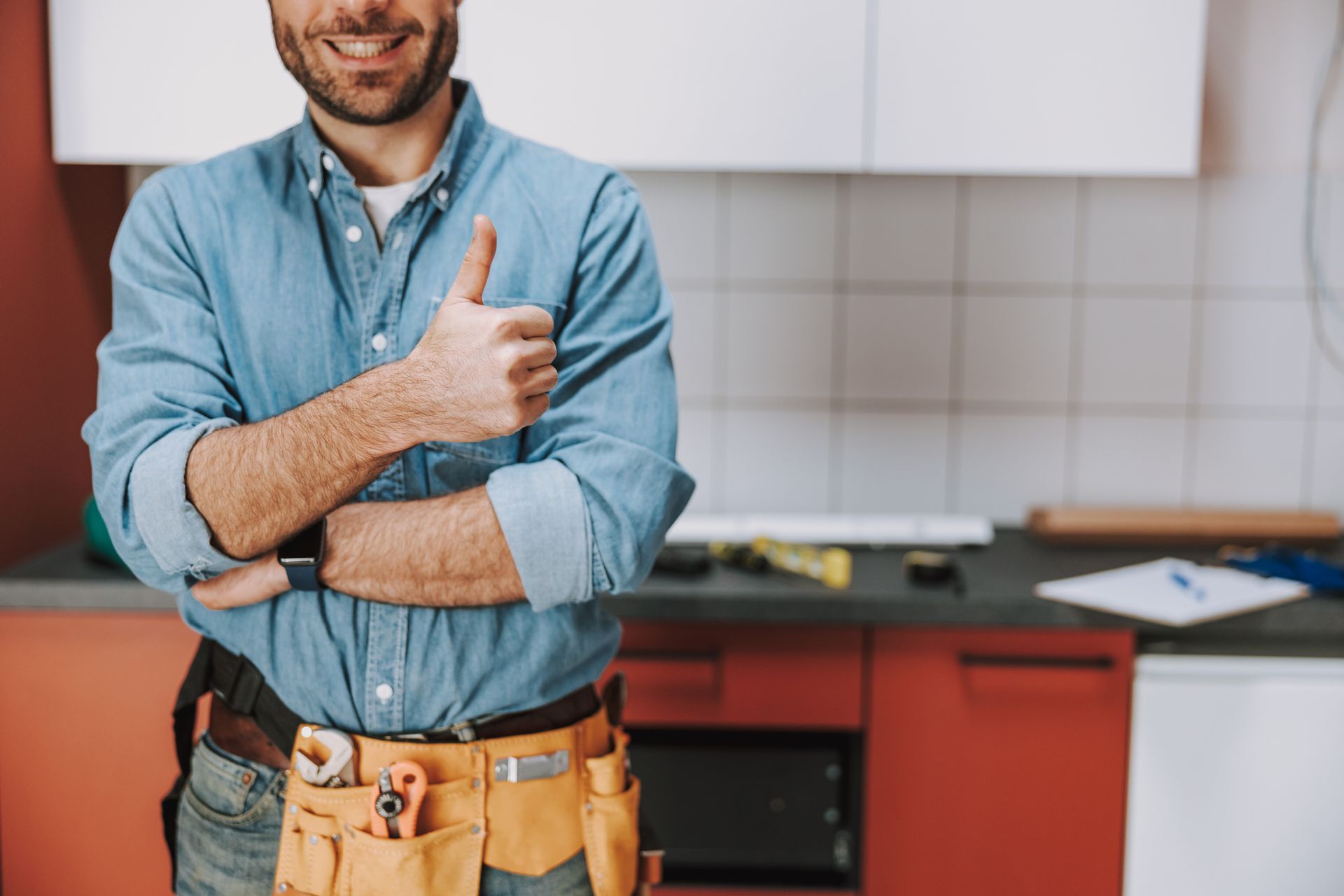 Contractor in blue shirt and tool belt giving a thumbs-up in a kitchen under renovation