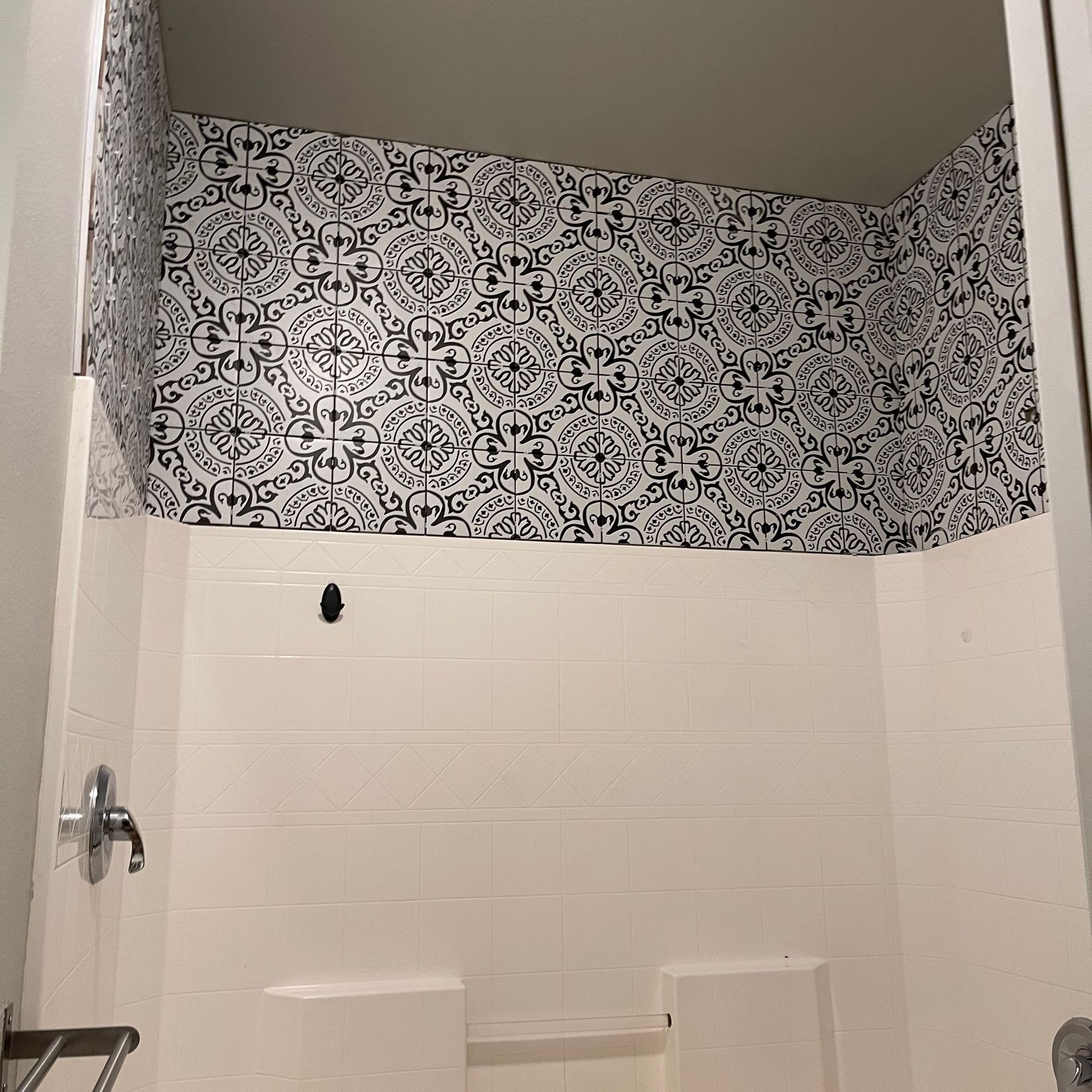 Bathroom shower/tub with white tile walls and black-and-white patterned wallpaper border above. Bathroom shower/tub with white tile walls and black-and-white patterned wallpaper border above.