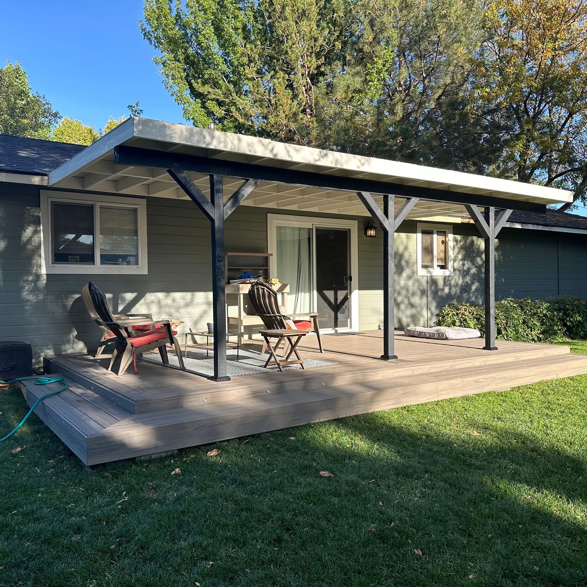Back patio with covered pergola, outdoor chairs, and table beside a house and grassy yard
