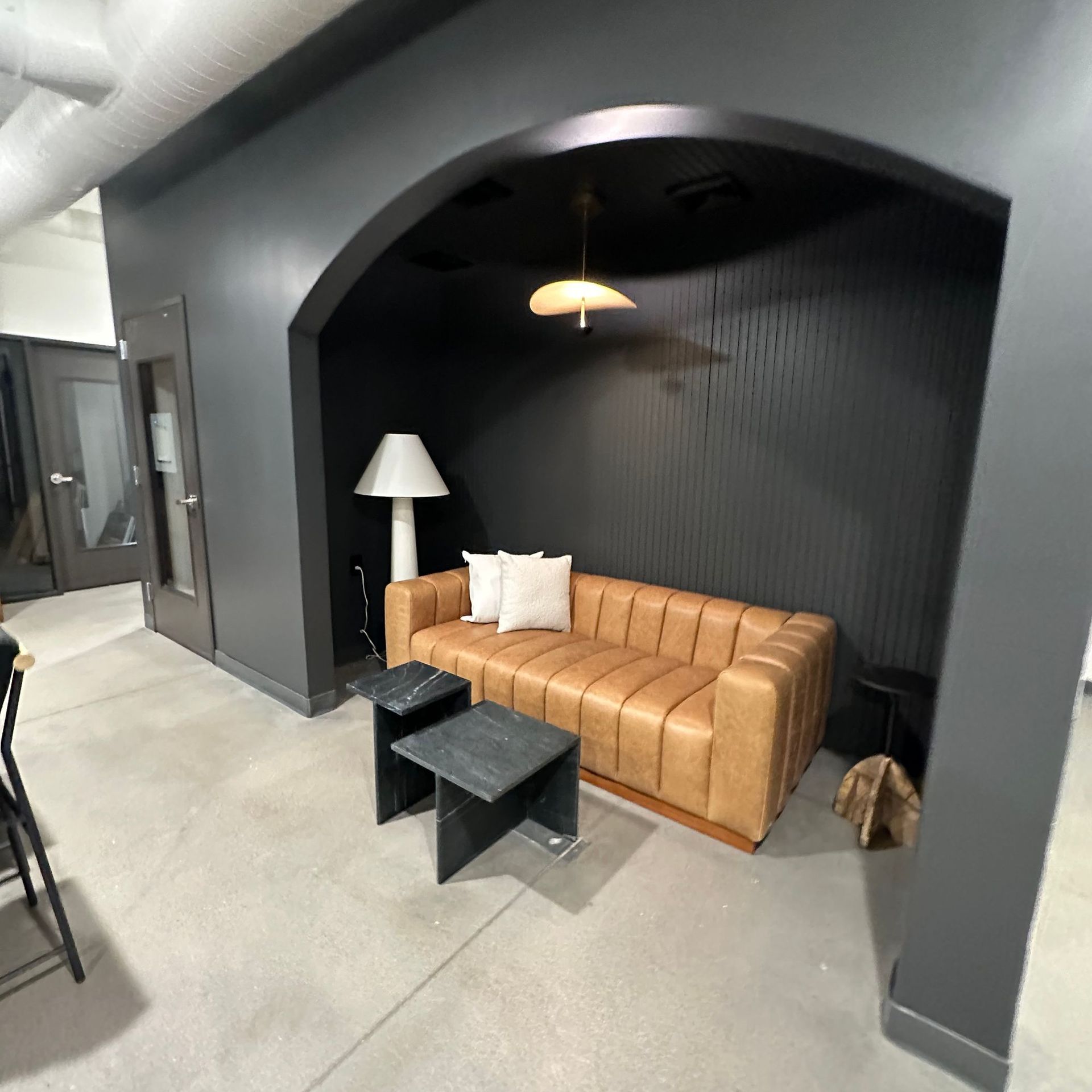 Modern lounge nook with tan sofa, black tables, floor lamp, and dark arched alcove wall.