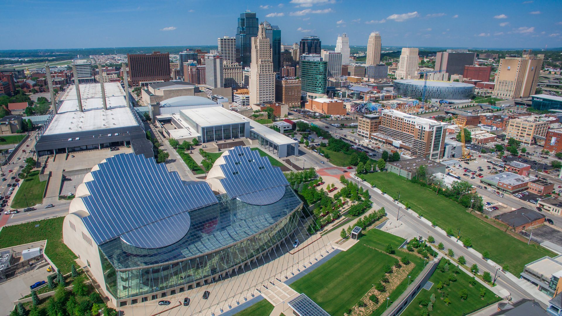 An aerial view of a city with a large building with solar panels on the roof.