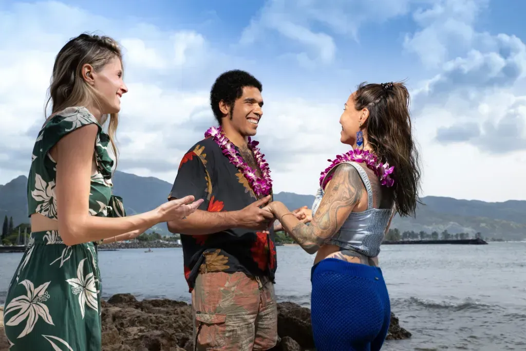 A man and two women are standing on the beach holding hands.