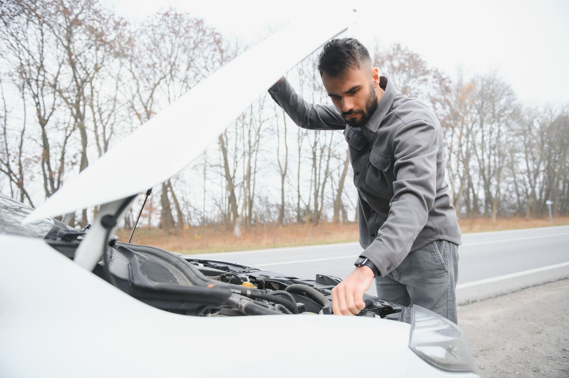 A man is looking under the hood of his broken down car.