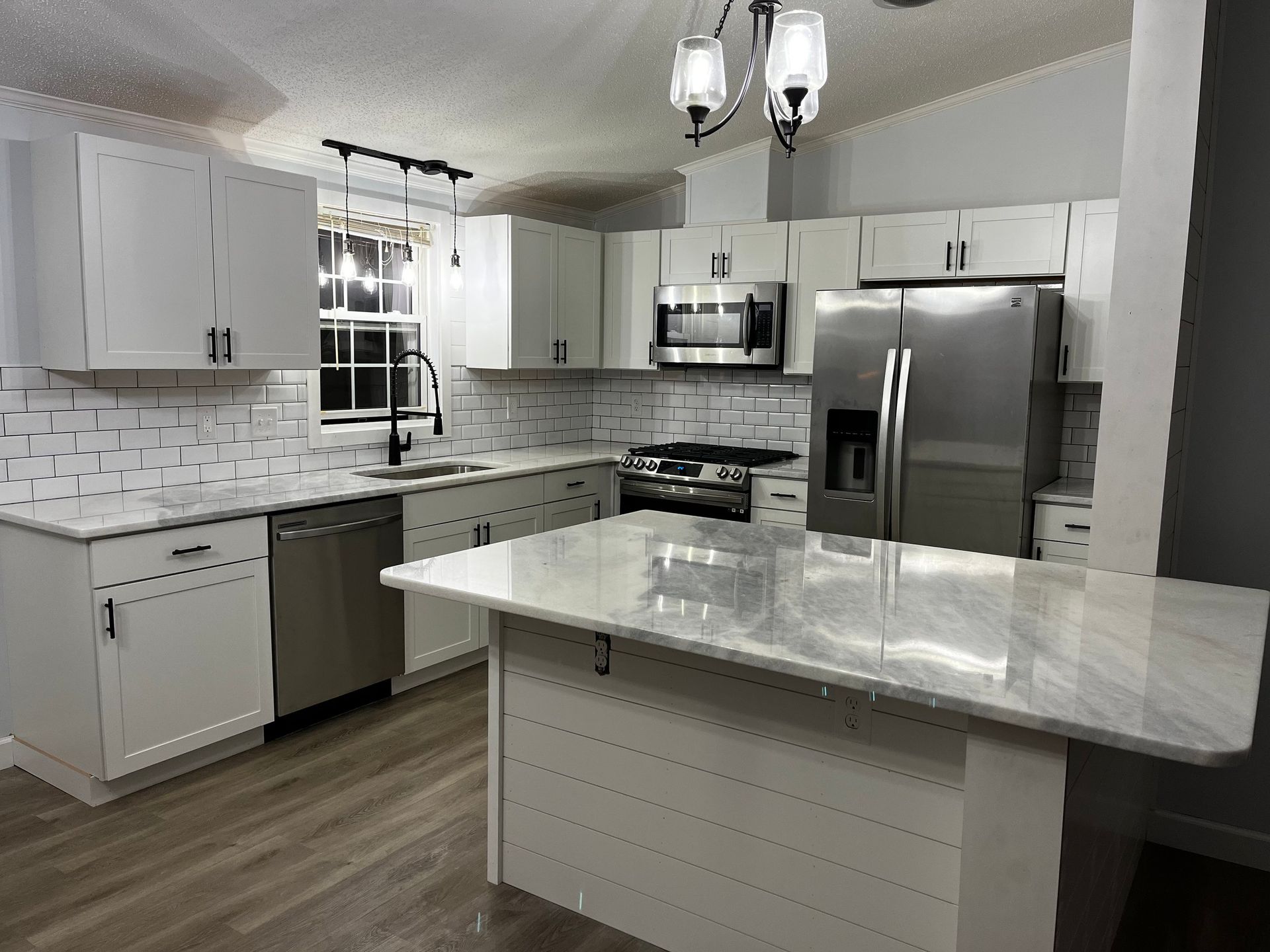 Bright modern kitchen with white cabinets, marble island, stainless steel appliances, and pendant lights.