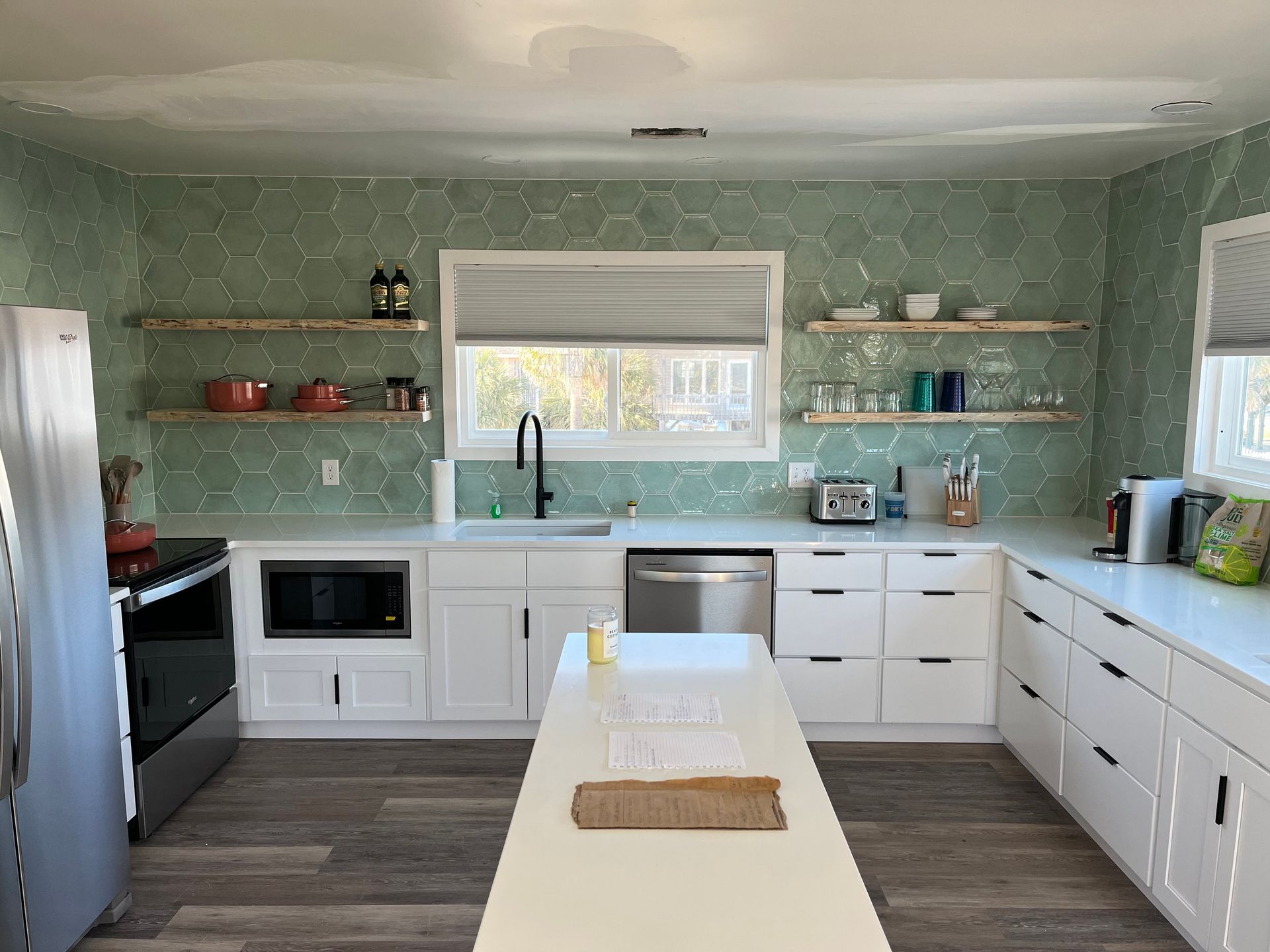 Bright modern kitchen with mint green walls, white cabinets, stainless appliances, and a central island with stools.