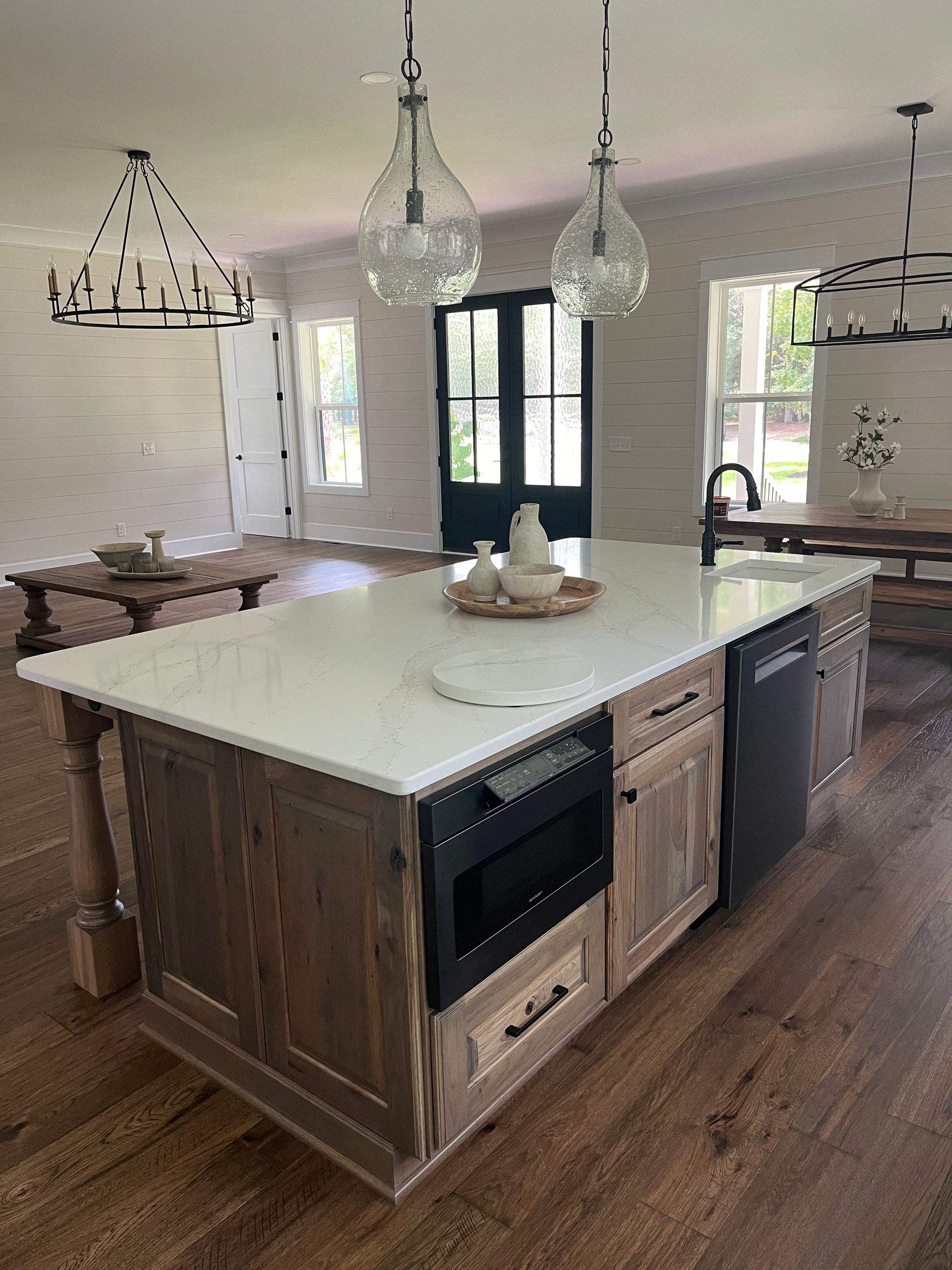 Modern kitchen with large white island, pendant lights, wood floor, and rustic cabinetry