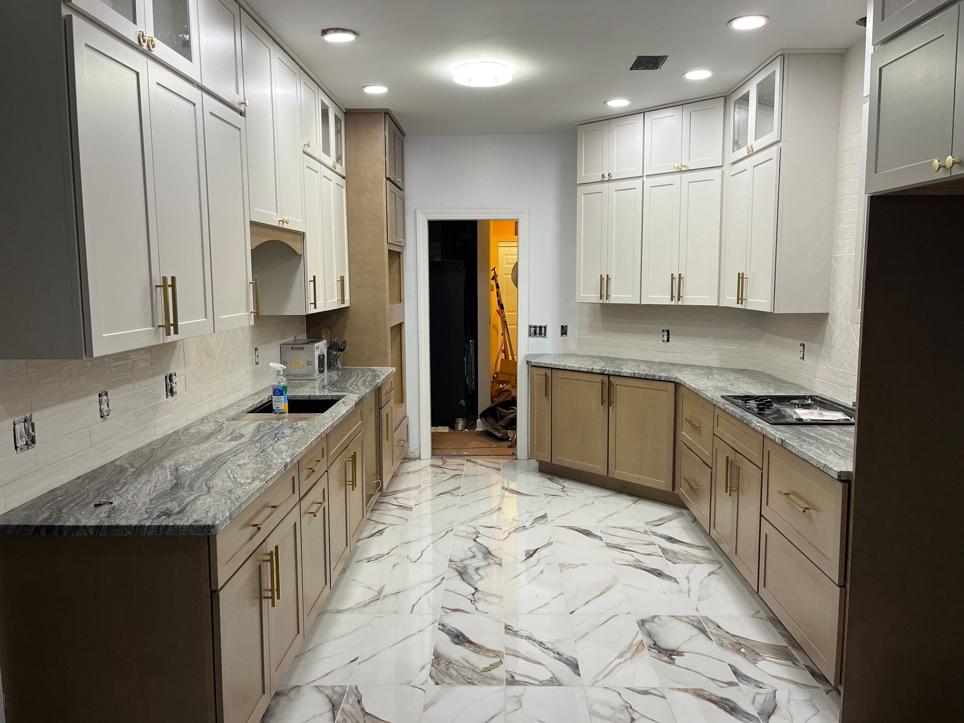 Bright modern kitchen with white cabinets, marble floors, and granite countertops, viewed down a narrow galley.