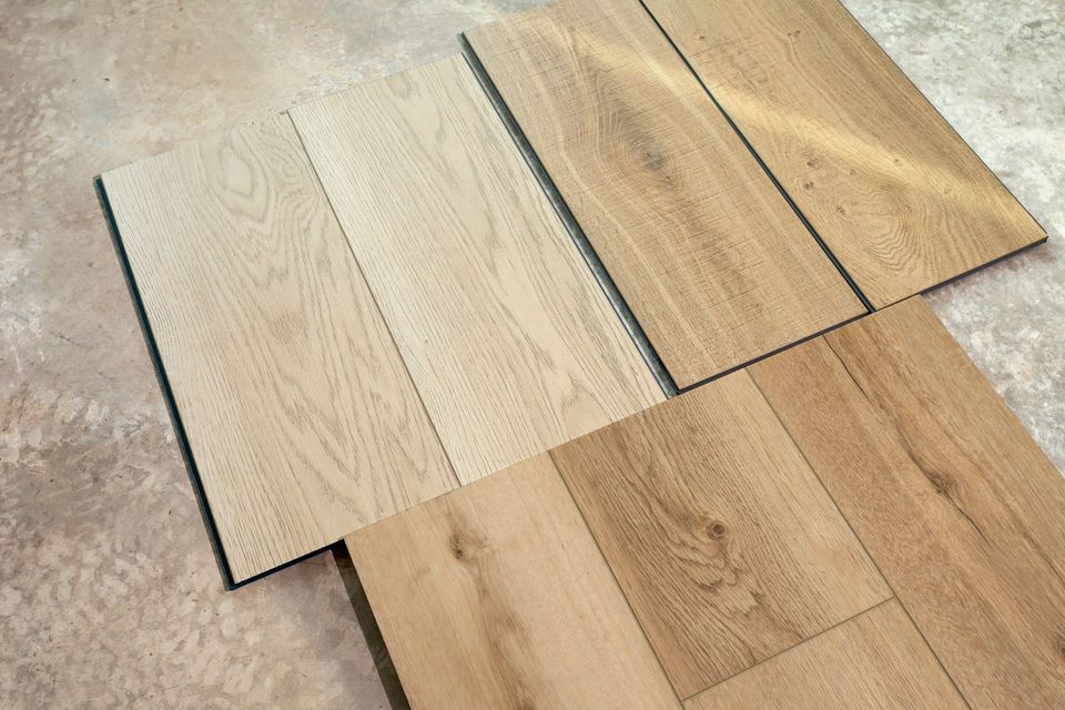 Sample wood flooring planks in light beige and brown tones laid out on a carpeted floor