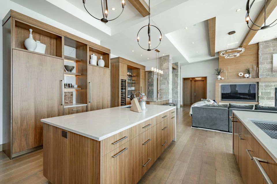 Modern open kitchen with wood cabinets, white island, pendant lights, and a gray living area beyond