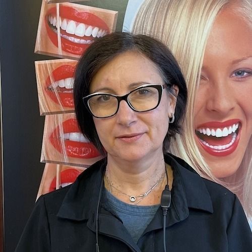 Woman wearing glasses standing in front of dental smile posters and a large smiling face display