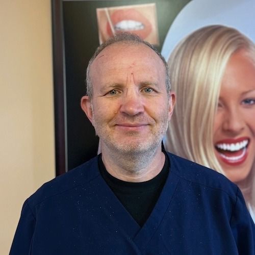 Man in dark blue scrubs smiling in front of a wall poster with a blonde woman's face.