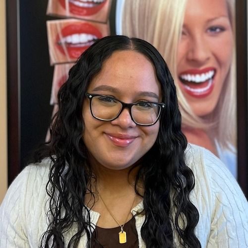 Woman with glasses smiling in front of dental posters with large toothy smiles