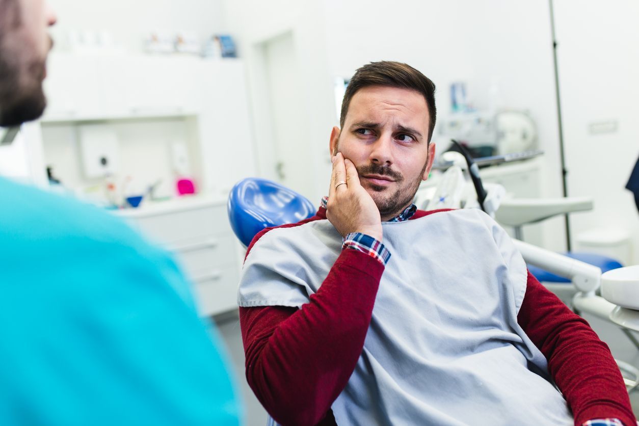 Patient touching his cheek while talking to a dentist in a clinic, wearing a blue bib