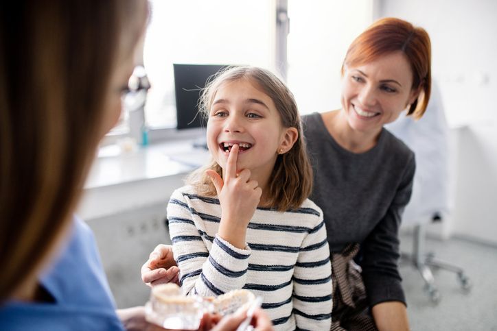 Child at a dentist visit smiling while a dentist and parent look on in a bright clinic