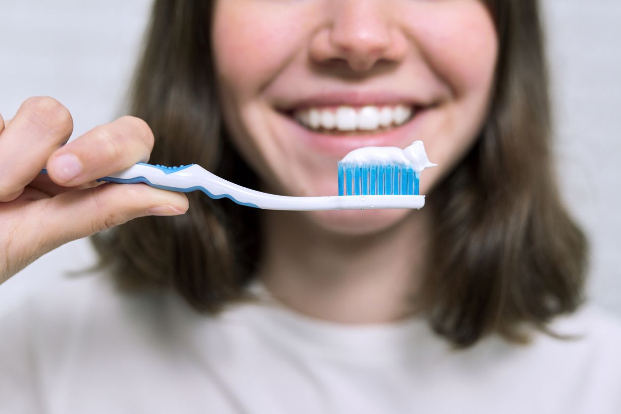Toothbrush with toothpaste in front of a smiling mouth