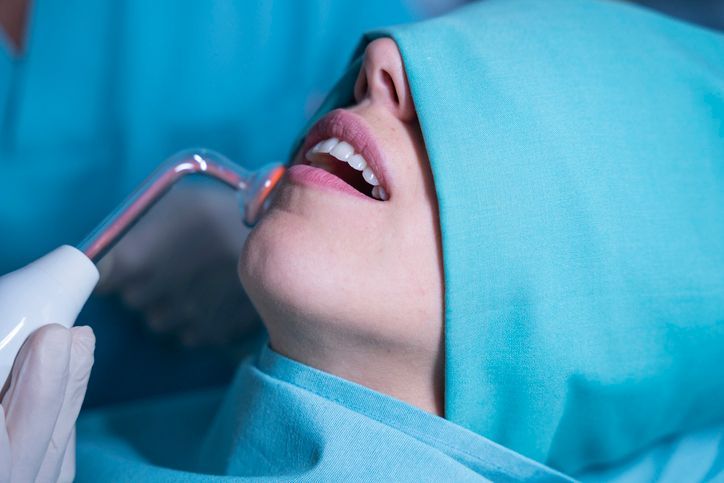 Dentist using a tool on a patient's open mouth during a dental procedure, with blue surgical drape.