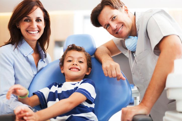 Dentist and assistant smiling with a child in a dental chair, showing a friendly clinic setting
