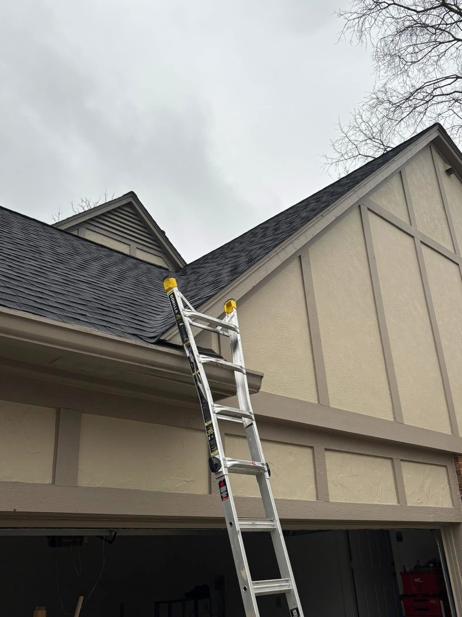 A person is standing on a ladder on the roof of a house.