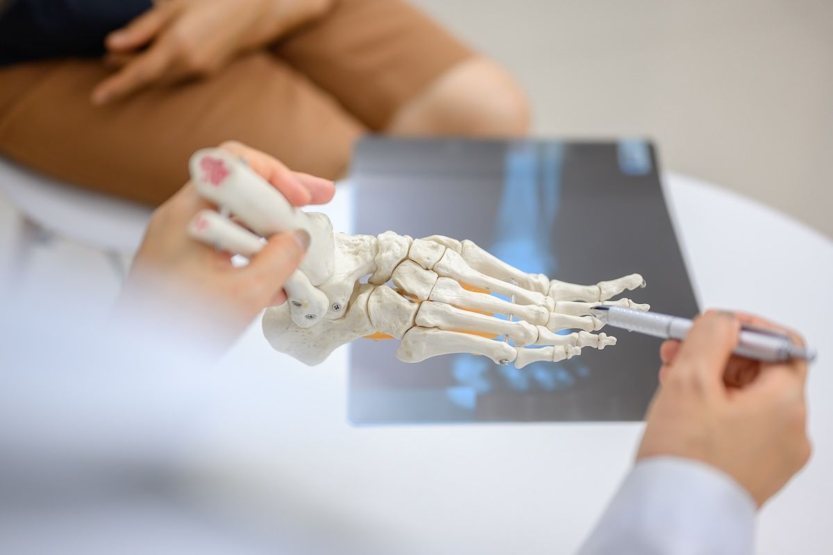 Close-up photo of an orthopedic doctor holding a model of ankle and foot bones explaining to a patie