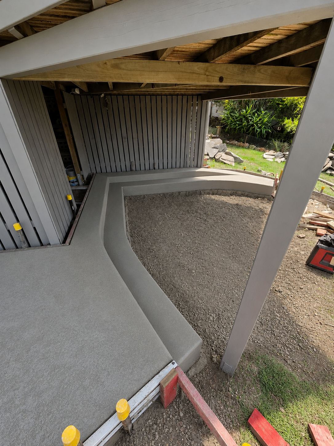 Covered outdoor ramp with curved concrete path, gray walls, gravel yard, and wooden roof beams — C & A Concreting In Craignish, QLD
